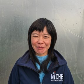 Woman smiling in a blue jacket against a foggy background.