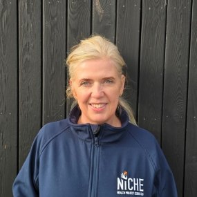 Smiling woman wearing a blue jacket against a dark background.