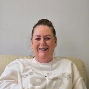 Smiling woman wearing a white sweater, seated comfortably.