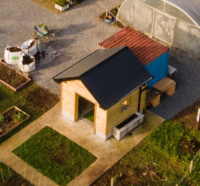 Small building with a black roof and surrounding garden plots.